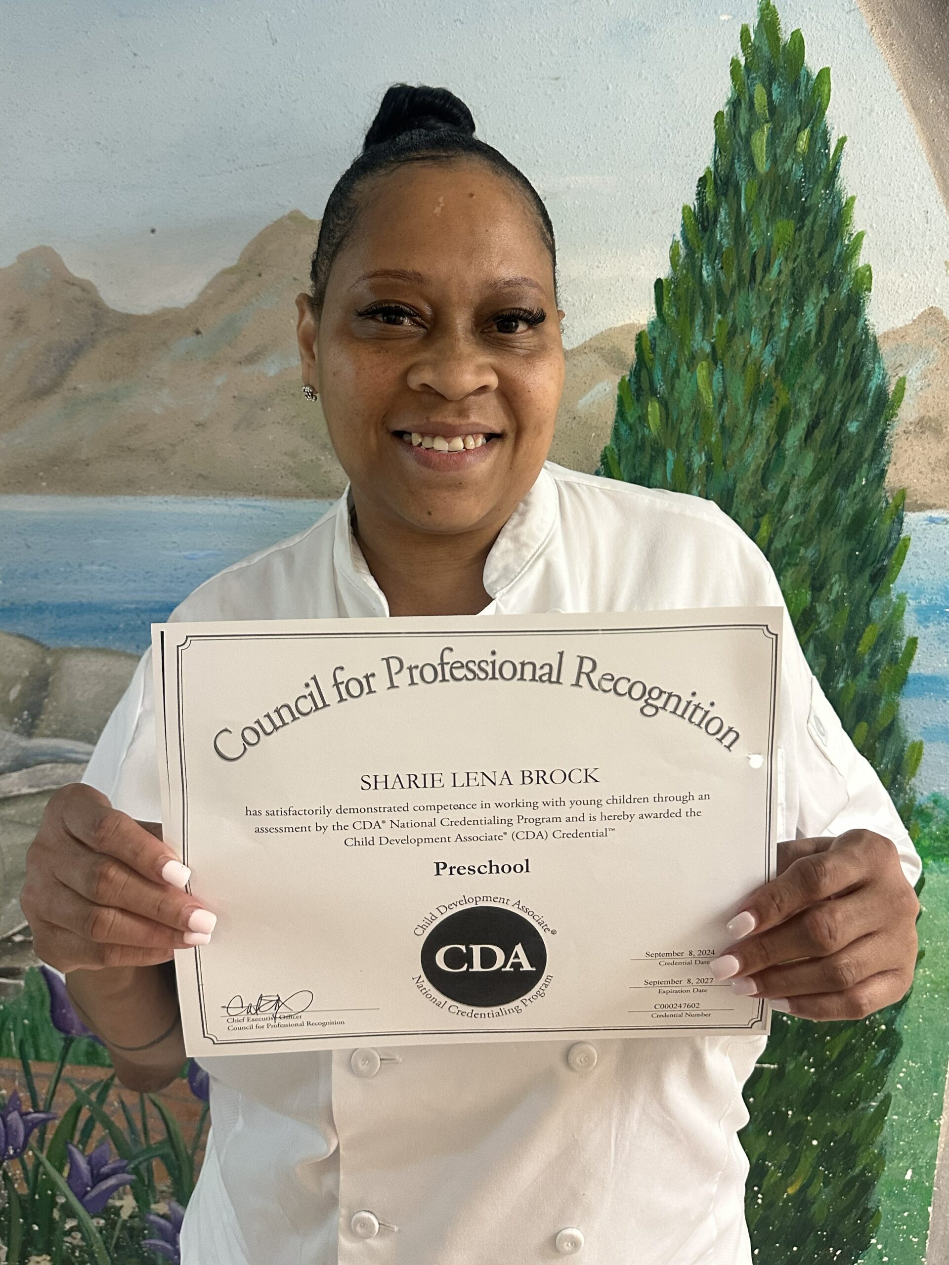 A happy Preschool CDA graduate, Sharie Brock, holding up her credentials for the camera.