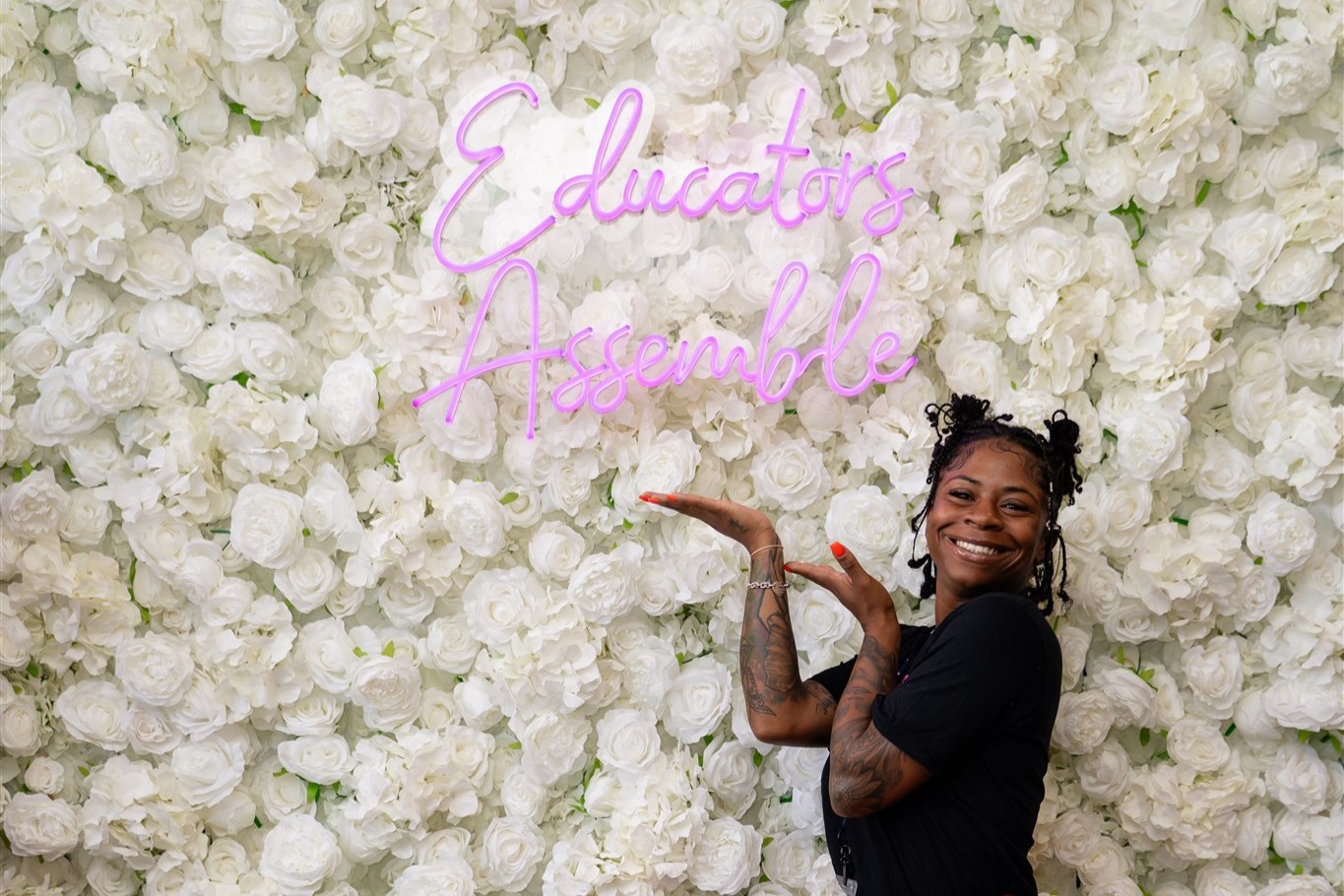 A young woman posing in front of the Educators Assemble™ signage.